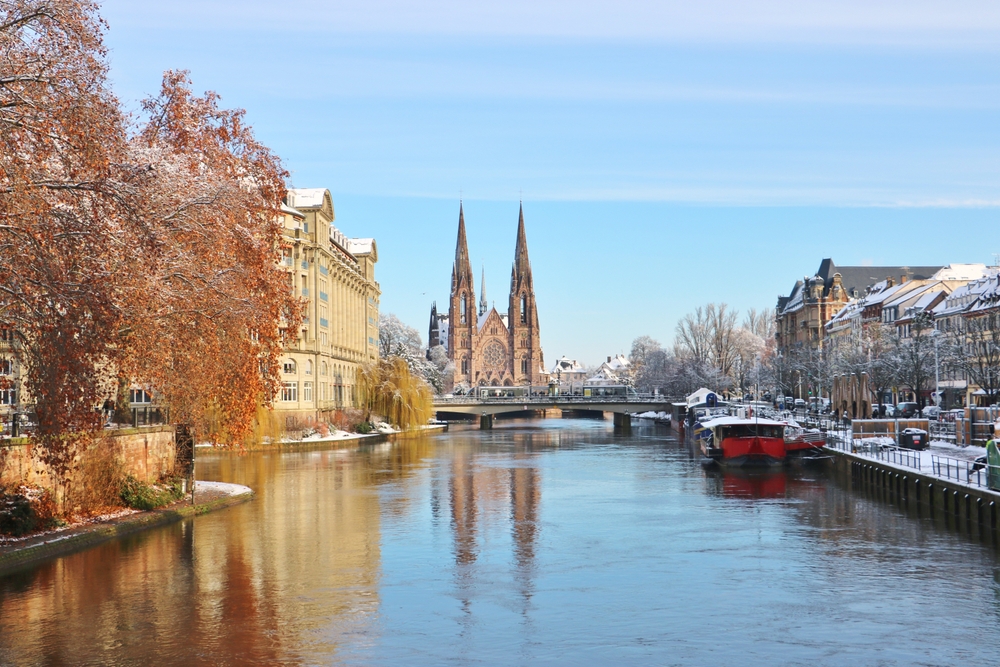 A view of the river in Strasbourg, with snow dusting the streets nearby and the cathedral in the distance