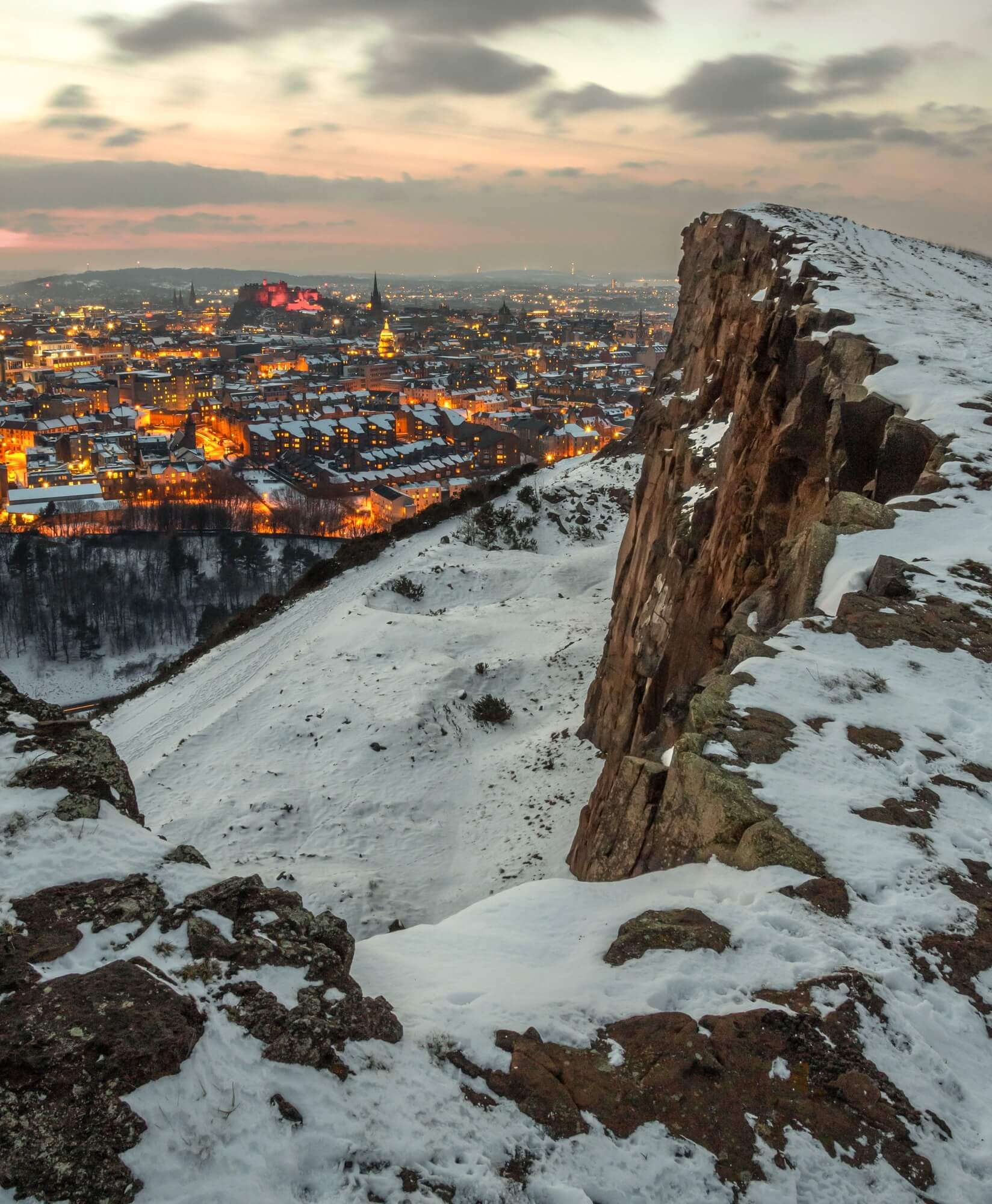 A snowy section of Arthur's Seat in Edinburgh, with the city below