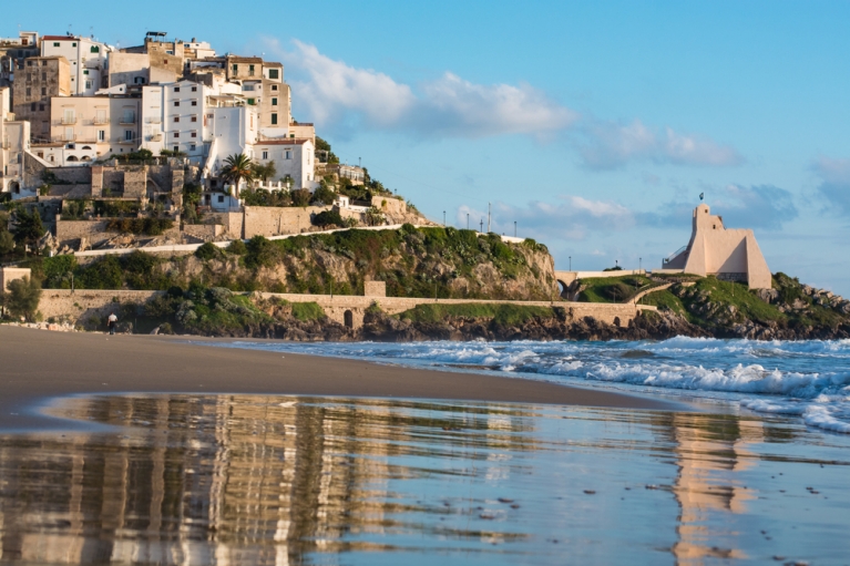 An empty beach with historic buildings on a hillside in the background