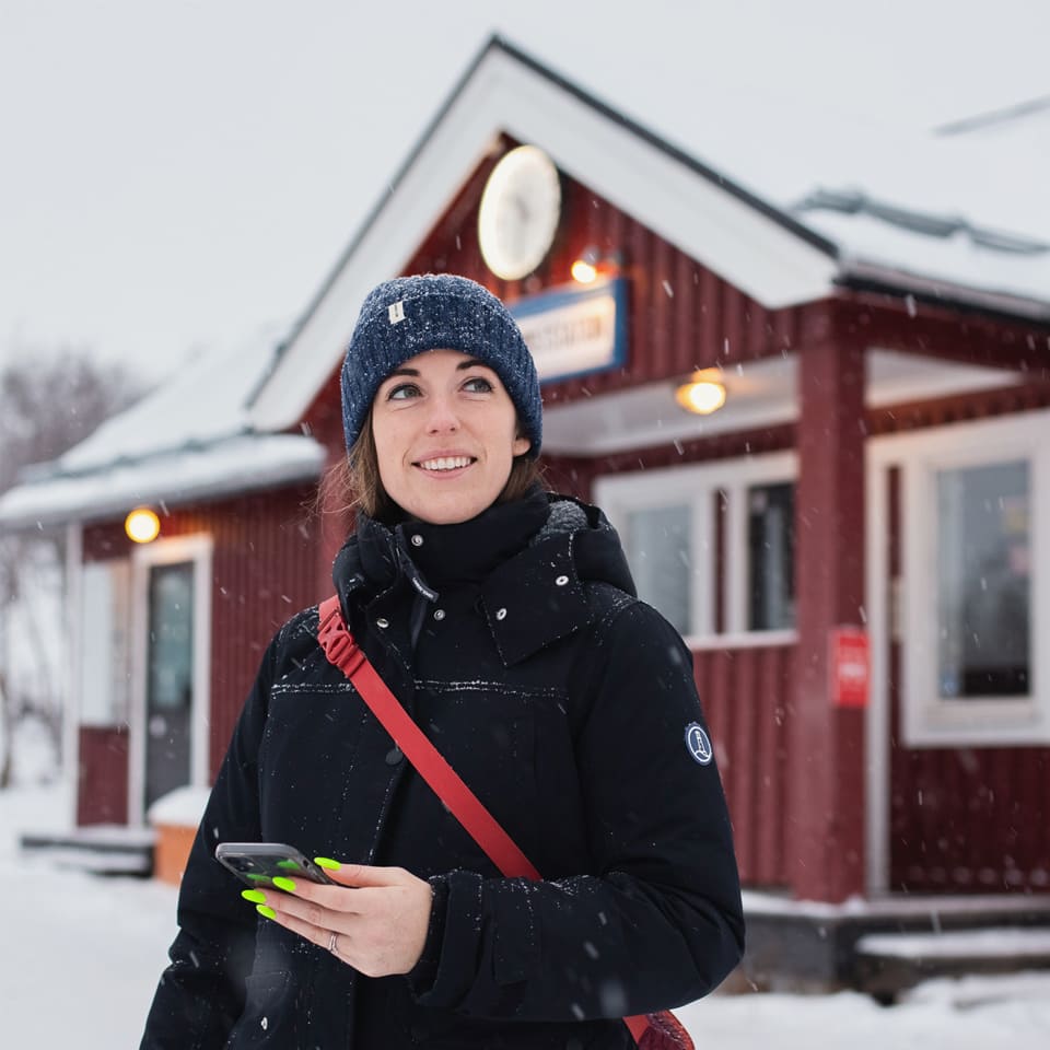 A woman stands outside a train station, looking at an approaching train