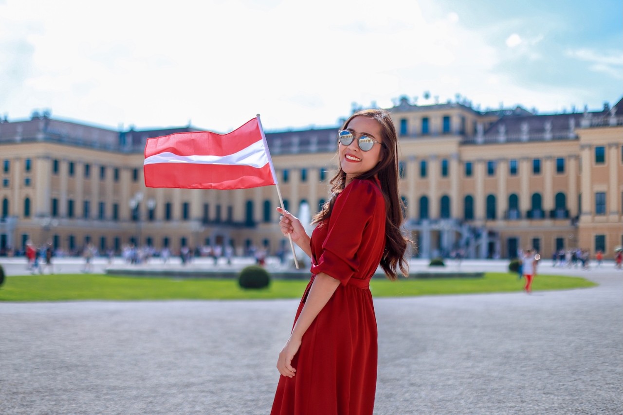 Tourist asian girl with Austria flag standing in front famous Schönbrunn palace in Vienna she looking at camera and smiling enjoying her vacation in the summer