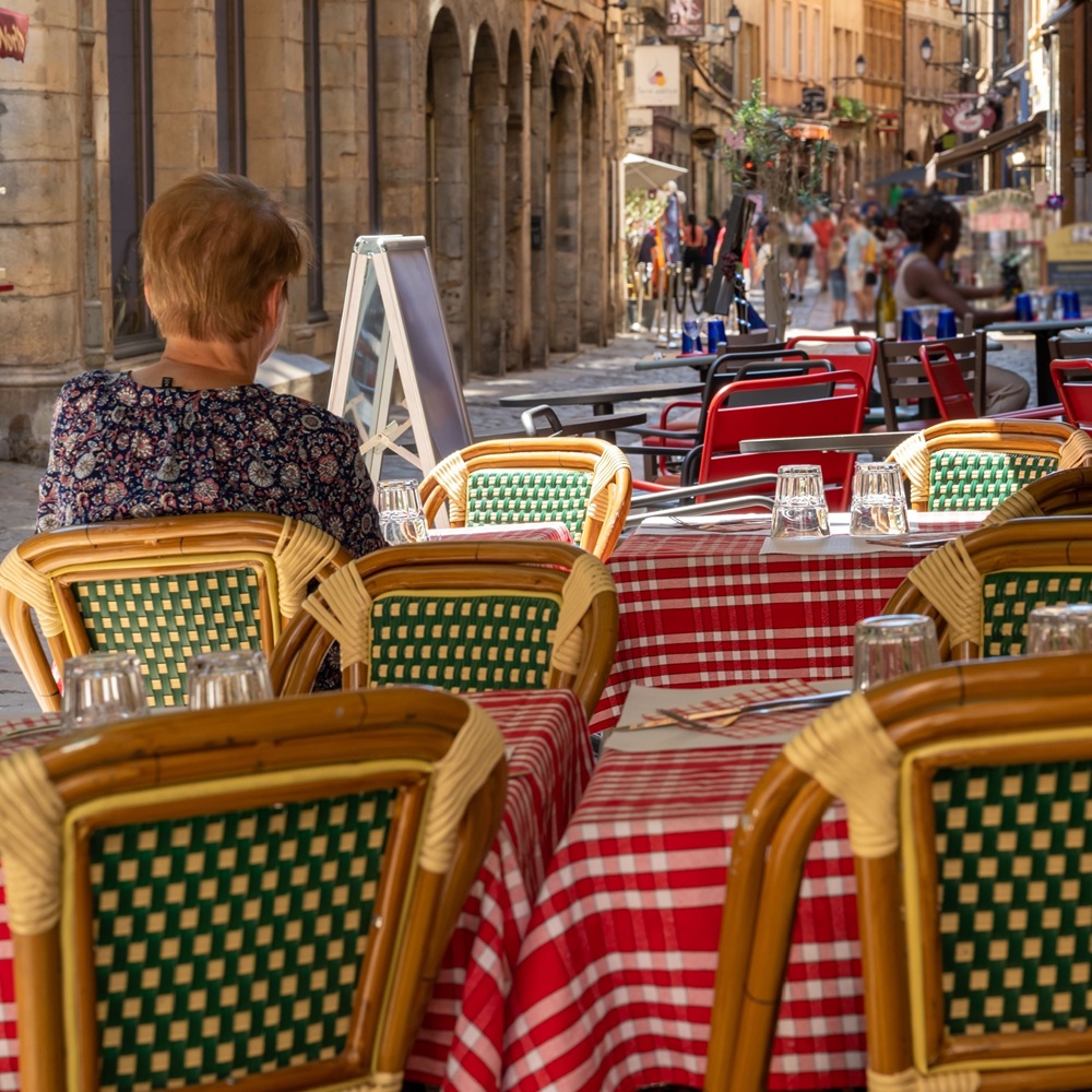 Una mujer sentada en una pequeña mesa al aire libre en un restaurante en Lyon