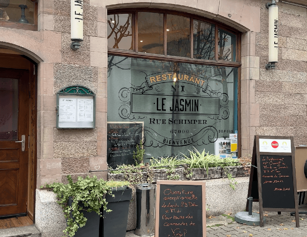 The exterior of Le Jasmin, on a quiet street. The restaurant's name and address is written in ornate font on the restaurant window