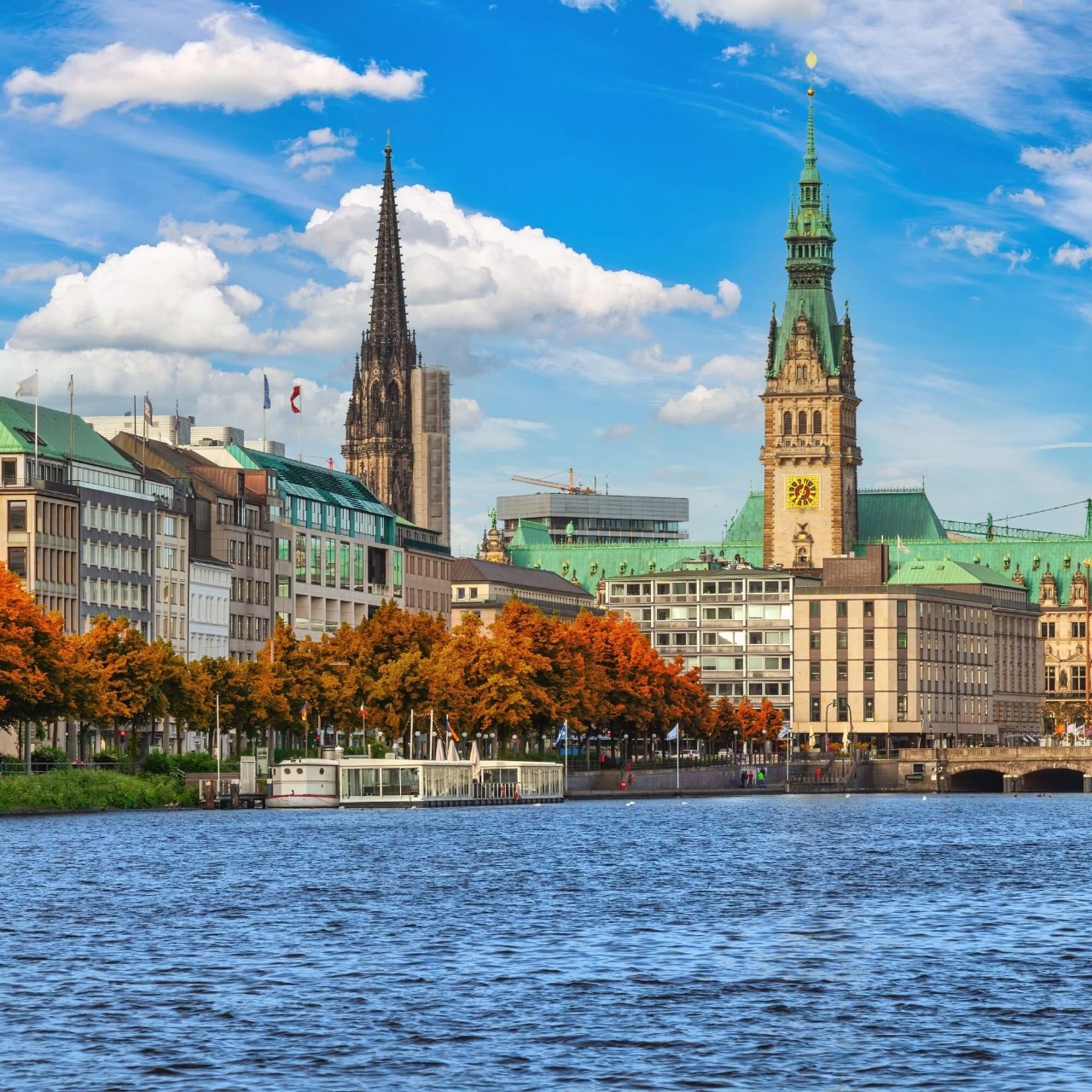 Uma imagem do lago de Hamburgo, com árvores de outono e edifícios históricos ao fundo